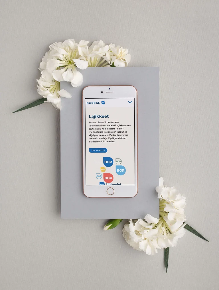 Kännykkä pöydän päällä kukkien vieressä.