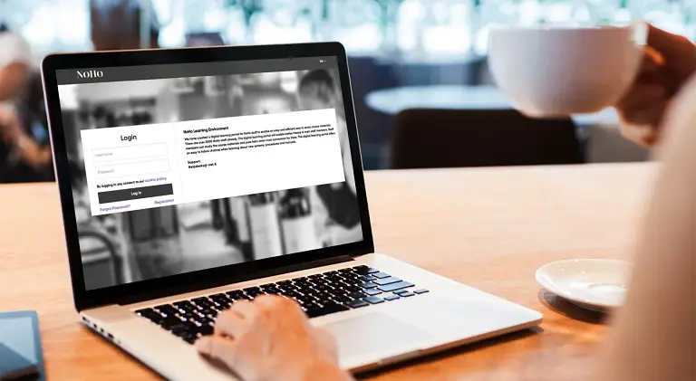 Henkilö istuu pöydän ääressä ja käyttää kannettavaa tietokonetta.