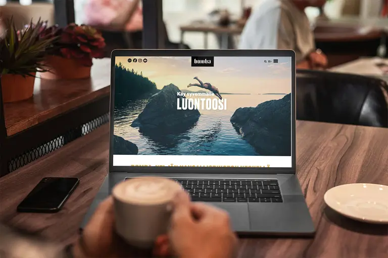 Henkilö istuu pöydän ääressä kannettavan tietokoneen ja kahvikupin kanssa.