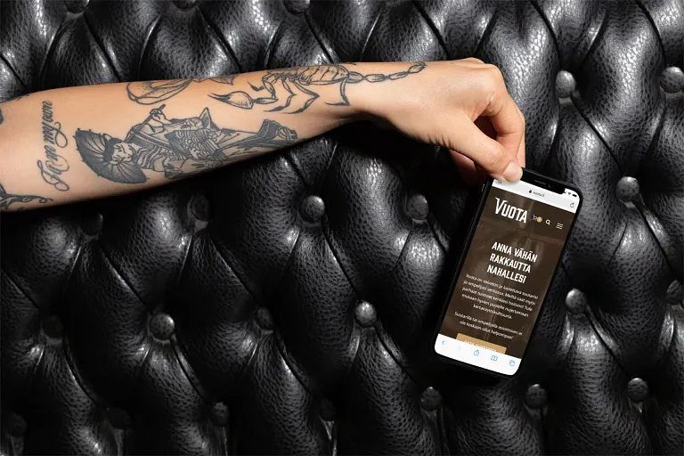 Henkilö, jolla on kännykkä kädessään ja tatuointi käsivarressa.