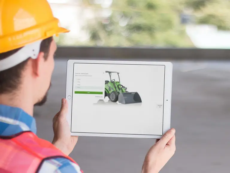 Kypäräpäinen mies, jolla on kädessään tabletti, jonka näytöllä näkyy rakennustyömaa.