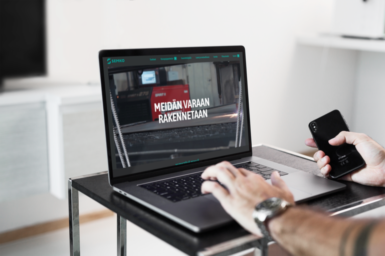 Macbookin näytöllä semkon sivustosta kuva, miehen käsi tietokoneen päällä